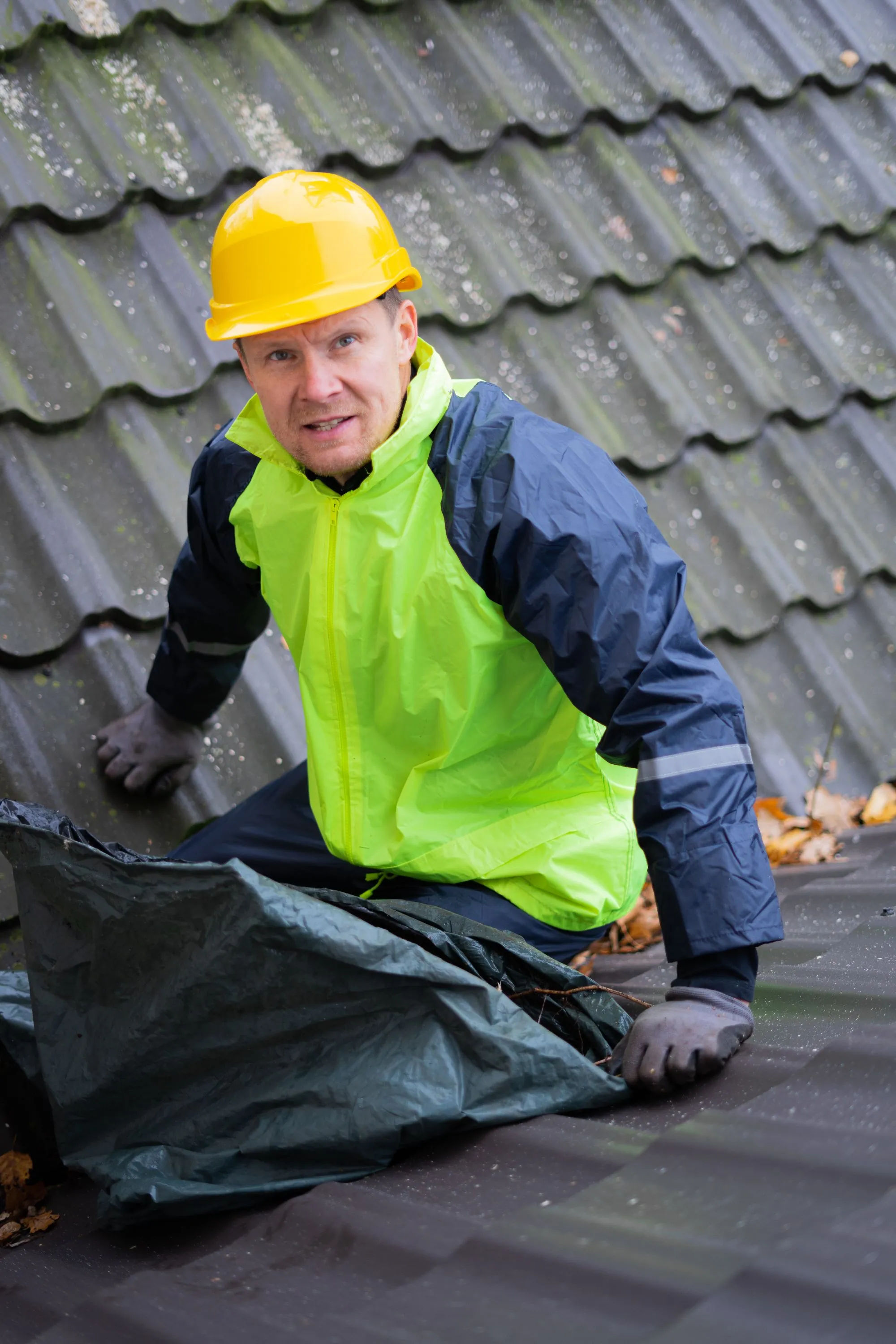 A roofer in a high-visibility jacket drawing a membrane across a wet roof