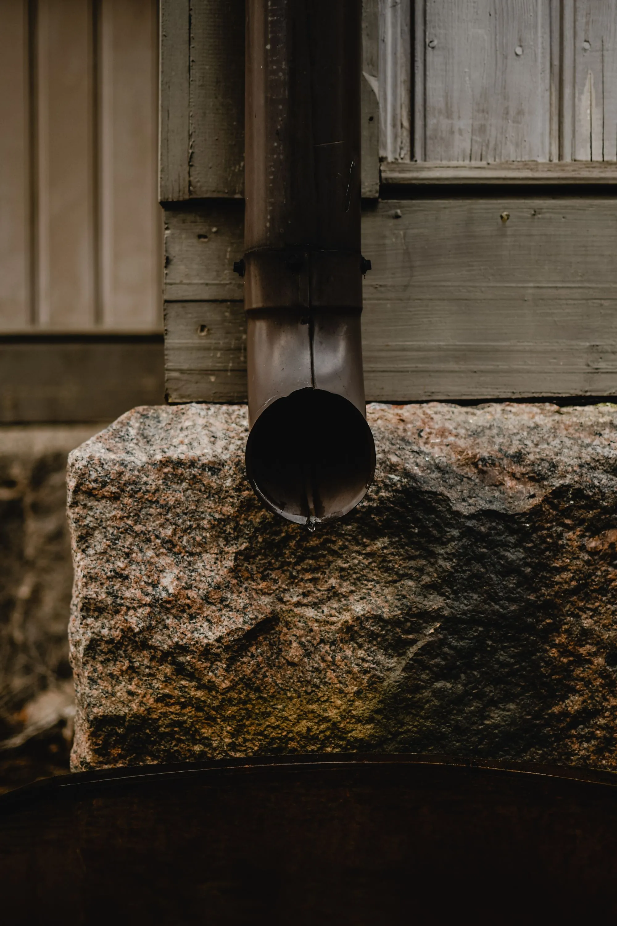 A downspout outlet discharging through a stone wall at ground level