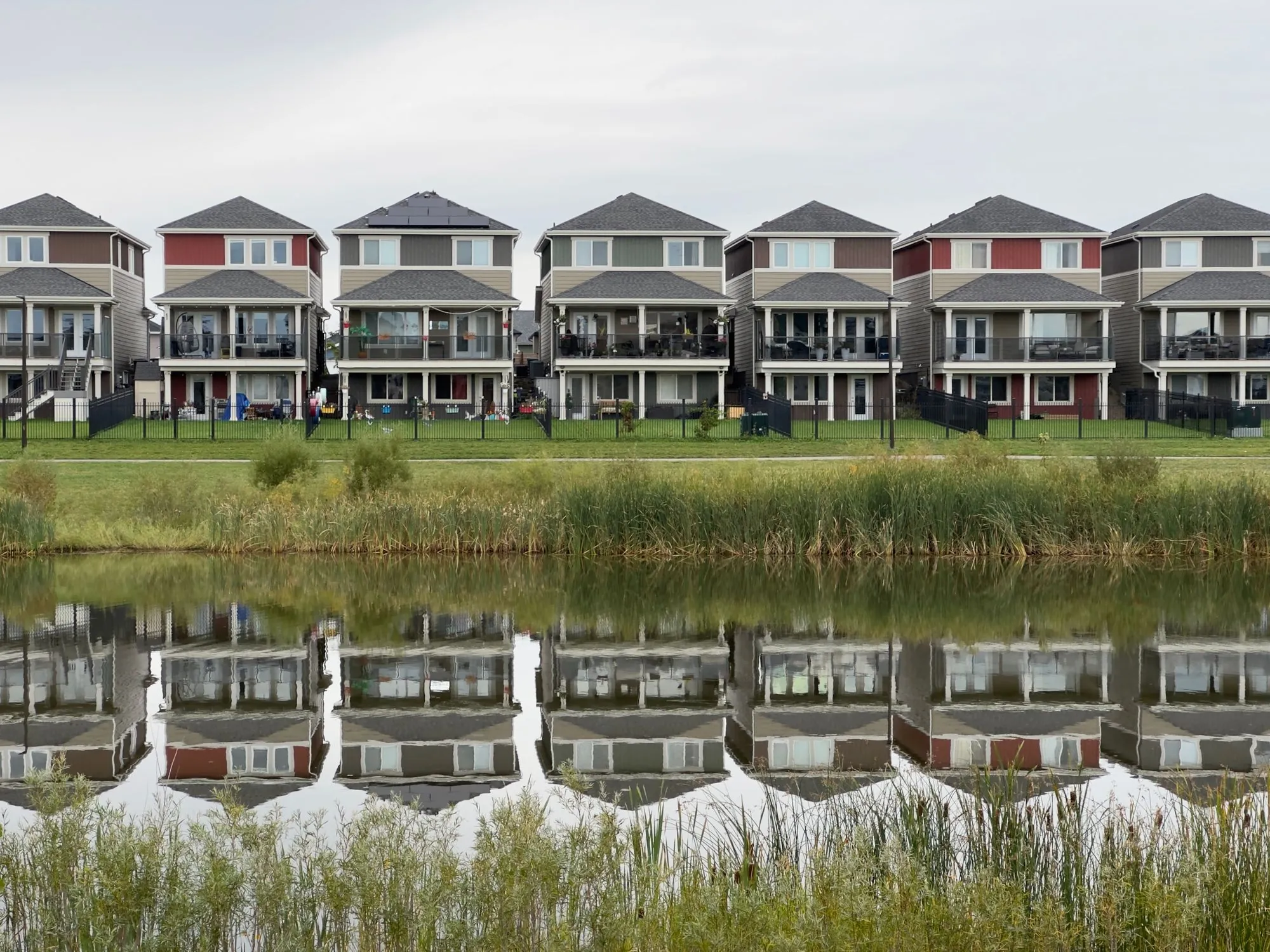 A row of pitched suburban houses reflected in the water in front of them