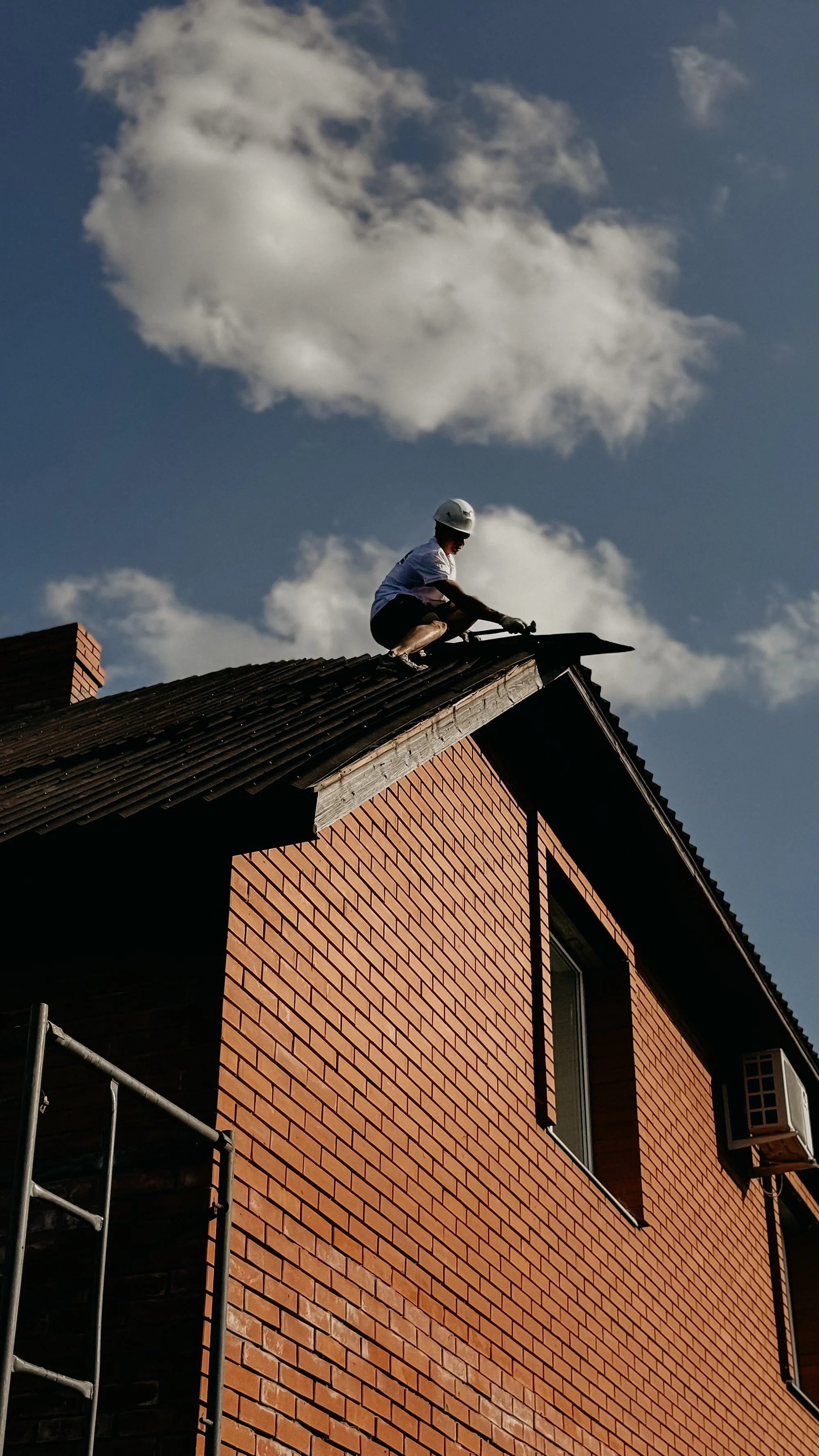 A roofer working along the gable slope of a house against an open sky