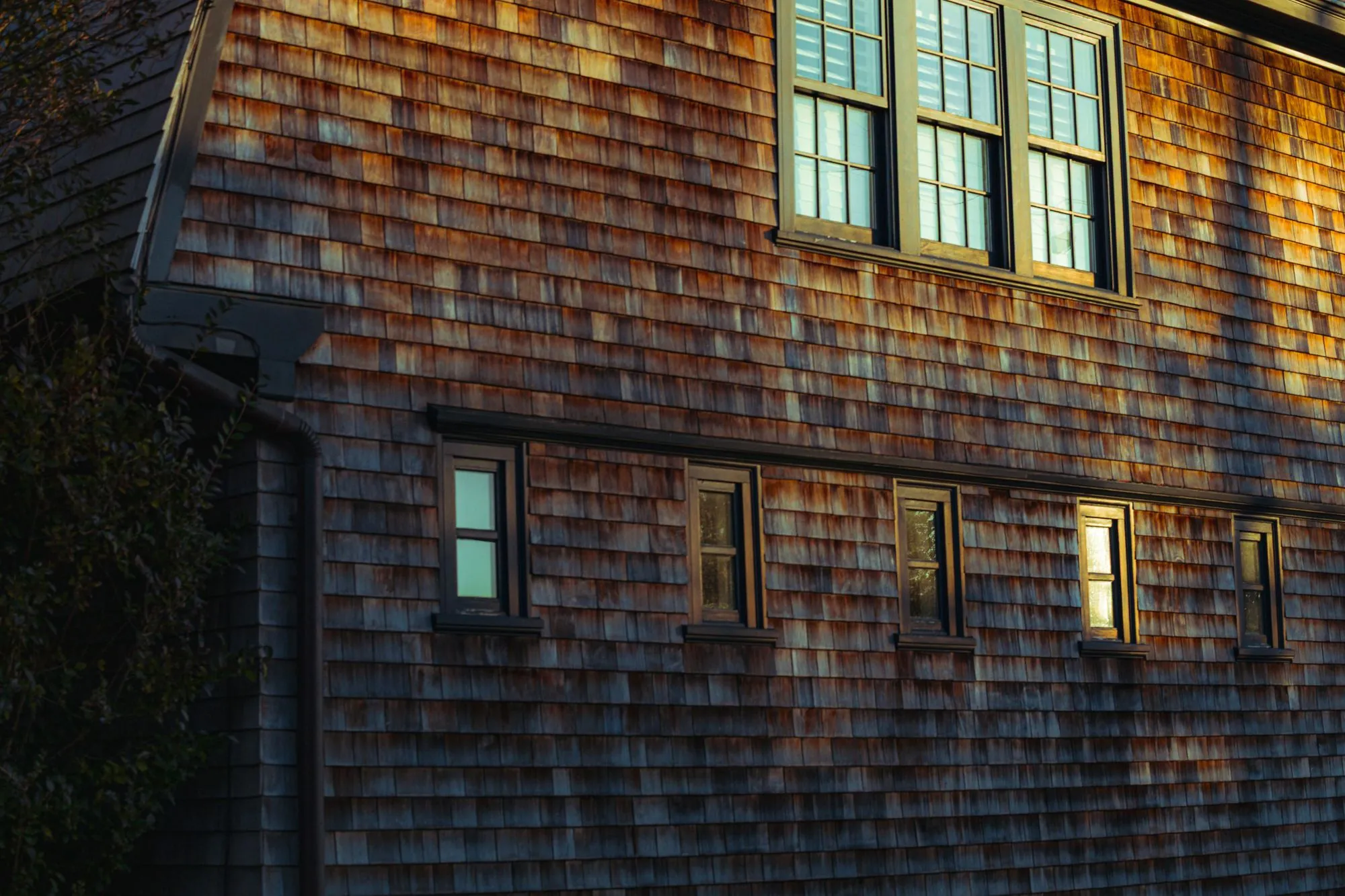 A cedar shingle house facade with white-framed windows in low sunlight
